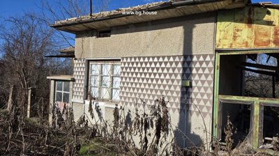 Close-up side view of the house showing patterned exterior walls, windows with metal grilles, and a rusty metal frame structure.