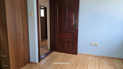Interior view of a room featuring a dark wooden door, a wooden wardrobe, light blue walls, and wooden flooring.