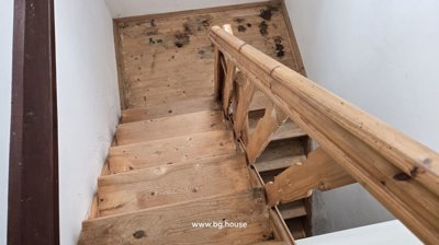 View of a wooden staircase with a simple wooden handrail and white painted walls.