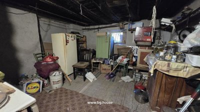 Interior of a storage room containing a refrigerator, several chairs, and assorted household items scattered around.