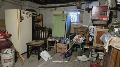 View of a storage room featuring a refrigerator, chairs, a broom, and boxes filled with various items.