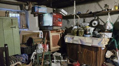 Interior of a storage room showing a microwave oven box, jars of preserved food, and a wooden kitchen cabinet.
