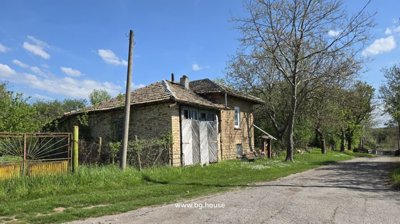 Side view of the brick house with wooden double doors and trees lining a village road