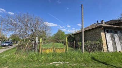 Rusty metal gate opening to a grassy garden area beside the brick house and trees