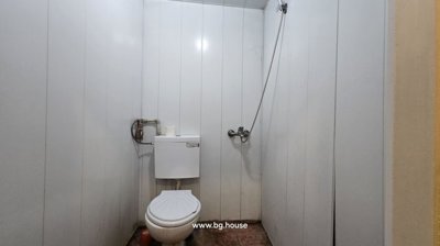 Compact bathroom featuring a toilet and wall-mounted shower head with white paneled walls.
