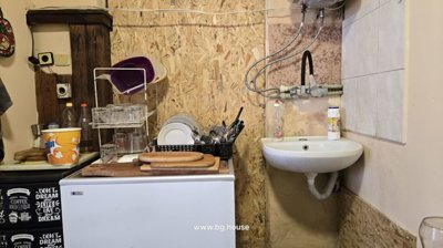 Small kitchen corner showing a sink, dish rack with glasses and utensils, and wooden wall paneling.