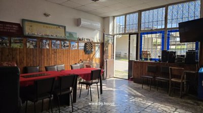 Spacious indoor area with tables covered in red cloth, chairs, large windows, and a dartboard on the wall.