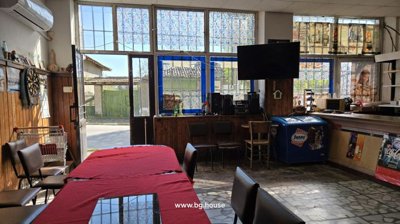 Interior view of a commercial space featuring tables, chairs, a counter, large windows, and a mounted TV screen.