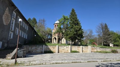 View of a small church with a bell tower surrounded by trees and a stone wall near the business complex