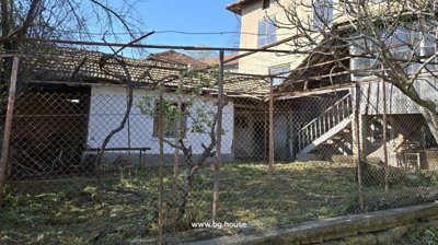Fenced garden area with a tree and a white building featuring external stairs