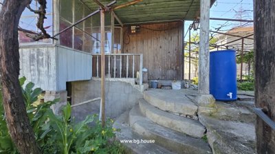 Concrete steps leading up to a wooden porch with a blue water barrel and garden tools.