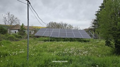 Photovoltaic solar panels mounted on a metal frame in a grassy garden area with trees and houses in the background.