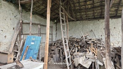 Covered storage space containing stacked firewood, wooden ladder, and various wooden items.