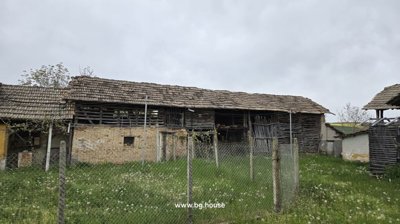 View of outbuildings featuring wooden slats and brick walls behind a wire fence in a green garden area
