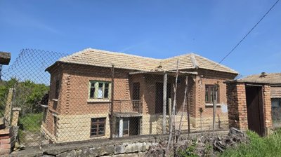 View of the house exterior with stone base and brick walls seen through a wire fence