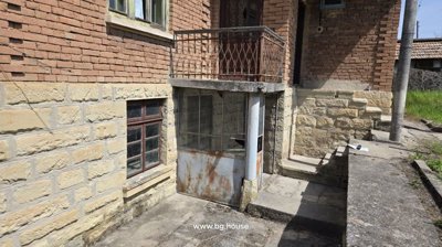 Basement entrance with rusted metal door and stone base beneath the house