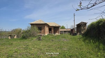 View of the Bulgarian house from the garden area showing grass, trees, and outbuilding