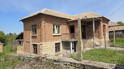 View showing the front and side of the house with stone base, brick walls, balcony, and entrance