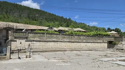 Decorative stone fence enclosing the garden area of the property, with pine forest visible on the hillside beyond.