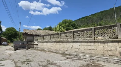 Stone fence running along a village street with pine forest covering the hillside behind the property.