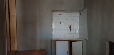 White tiled niche with a rusty tap and wooden cabinet doors beneath in an interior room with plain walls