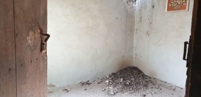 Interior room showing an open wooden door, plain walls, and a pile of dirt or debris on the floor