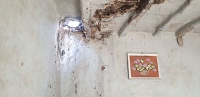 Interior ceiling with visible damage and a small round hole, alongside a framed picture of flowers on the wall
