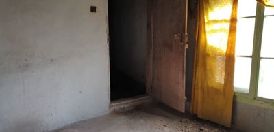 Interior room showing an open wooden door, a window with a yellow curtain, and plain walls