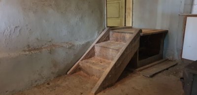 Interior room showing plastered walls, a small wooden staircase, and an open doorway leading to another space.