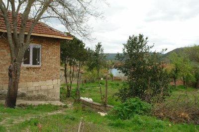 Corner view of a rural brick and stone house surrounded by trees and grass in Svalenik village.