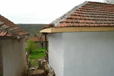Side view of a white plastered rural house featuring a tiled roof and wooden eaves.