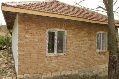 Brick wall section of a rural house showing two windows and a tiled roof above.