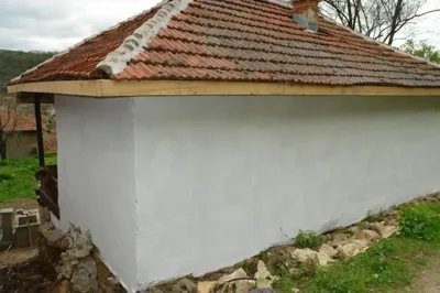 Side view of the rural house featuring a white plastered wall and a tiled roof above.
