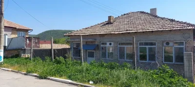 Exterior of a single-storey brick house with multiple windows, a tiled roof, and a fenced yard with greenery.
