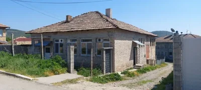 Side view of a brick house with multiple windows and a fenced yard alongside a dirt road