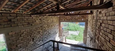 Inside view of an unfinished brick structure showing roof beams and an open entrance to the yard