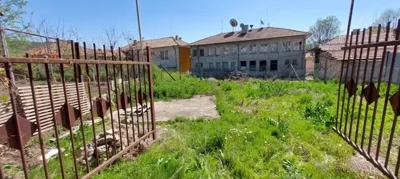 View of a grassy yard enclosed by a metal gate with neighboring buildings in the background
