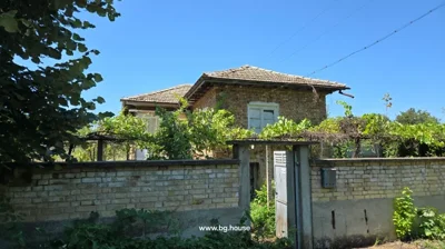 Two-story brick house with tiled roof behind a brick wall with metal gate and green vines growing on trellis