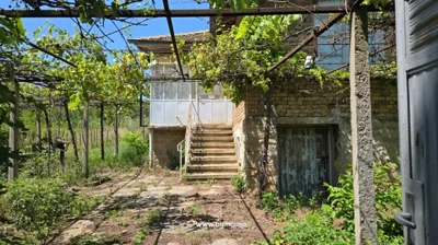 Concrete stairs leading up to a two-story brick house with a tiled roof, surrounded by greenery and a paved area.