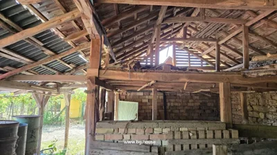 Interior of a rustic covered area showing wooden beams, brick walls, and various stored items including barrels and wooden pallets