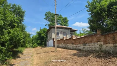 Two-story house with decorative walls, tiled roof, brick and stone fence, dirt path, and greenery.