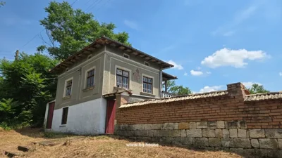 Two-story house with windows, decorative horse figure, tiled roof, brick and stone fence, greenery.
