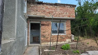 Brick extension of the house with window and open doorway next to a larger building facade.