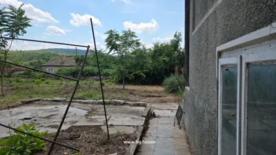 Garden area featuring a concrete path, metal frame structure, trees, and bushes under a partly cloudy sky.