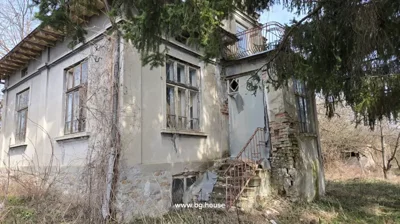 Side view of an old house showing cracked walls, broken windows, and dry vegetation around