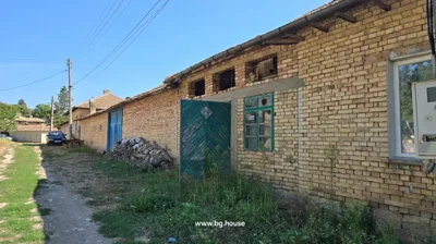 Long brick building with blue wooden doors, green gate, and dirt path alongside