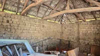 Room with mud brick walls, wooden roof structure, and assorted items including windows and furniture parts