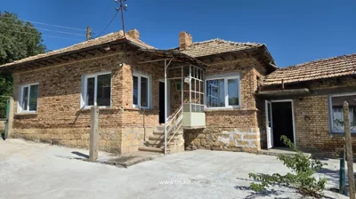 Brick house with tiled roof, white framed windows, entrance with stairs and metal railing, concrete yard in front under clear blue sky