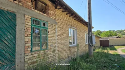 Close-up view of brick house wall showing green wooden door, window with glass panes, and electrical box mounted on wall