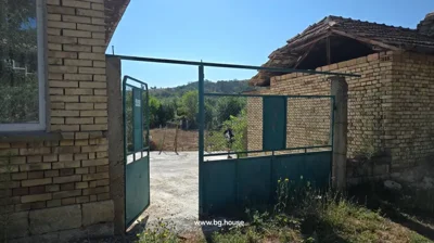 Open green metal gate attached to brick walls, view into concrete yard with person standing in background